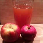 Zwei Äpfel vor einem Glas mit frischem Apfelsaft.